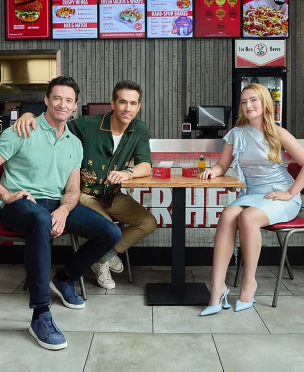 Three people sitting at a table in a fast-food restaurant with menu boards in the background.
